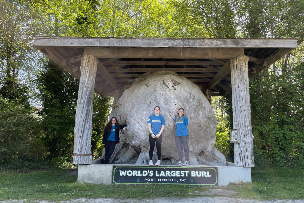 The Port McNeill tourism staff pose in front of the World's Largest Burl landmark on North Vancouver Island.