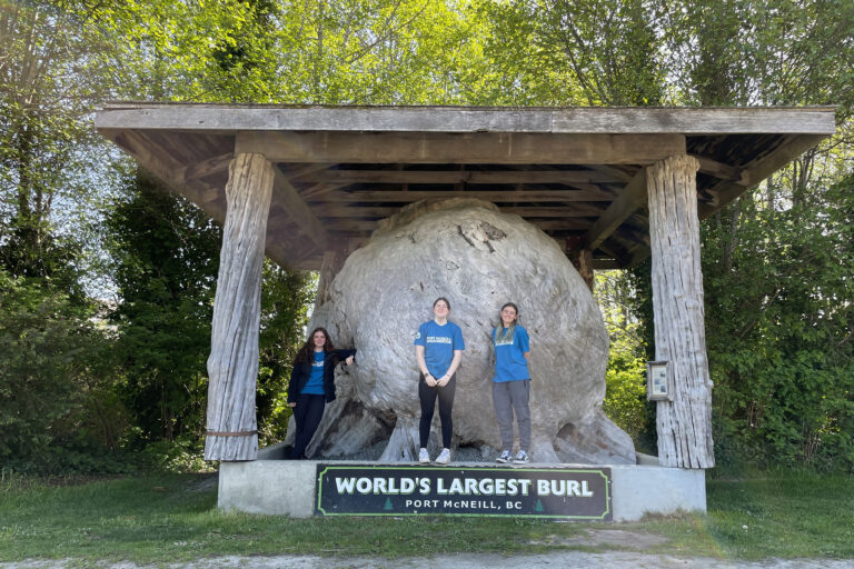 The Port McNeill tourism staff pose in front of the World's Largest Burl landmark on North Vancouver Island.