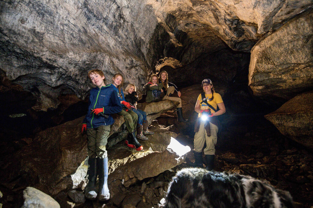 A group of hikers, of all ages from young kids to grandparents, explore the Upana Caves with their handheld flashlights.